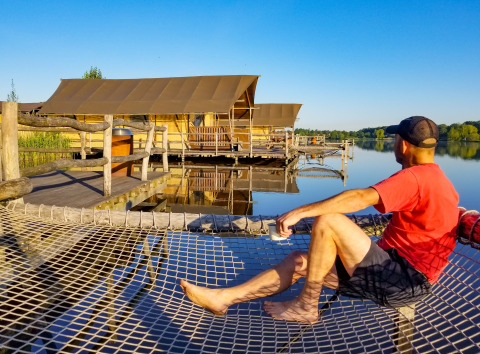 Man relaxing with a coffee on a net hammock in front of WaterLodges at Recreatiepark TerSpegelt, Brabant.
