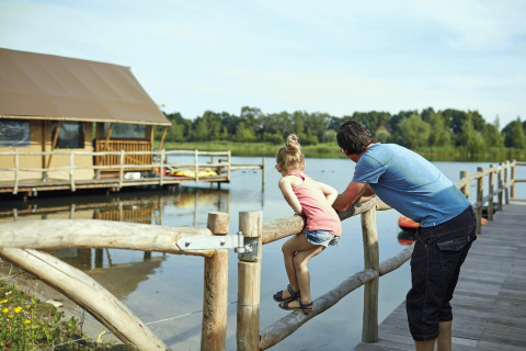 Padre e figlia su un pontile di legno vicino a una tenda glamping al Recreatiepark TerSpegelt - WaterLodges Brabant.