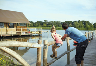 Vater und Tochter auf einem Holzsteg am Wasser mit Glamping-Zelt bei Recreatiepark TerSpegelt - WaterLodges Brabant.