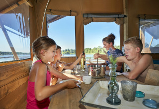 Familie nyder måltid sammen i glamping telt ved søen på Recreatiepark TerSpegelt WaterLodges Brabant.