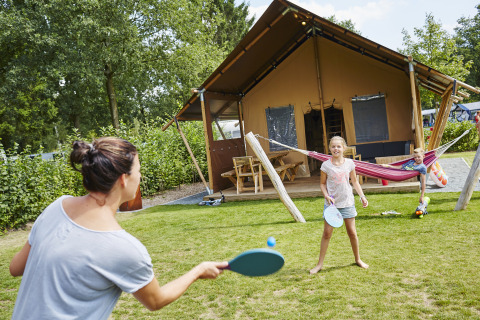 Famiglia che gioca a racchettoni davanti a tenda glamping presso Recreatiepark TerSpegelt WaterLodges Brabant.