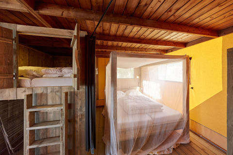 Interieur van WaterLodges Brabant glamping met hemelbed met muskietennet en een houten stapelbed.