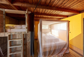 Interieur van WaterLodges Brabant glamping met hemelbed met muskietennet en een houten stapelbed.