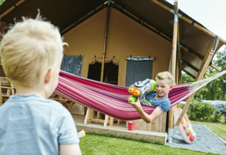 Niños jugando con pistola de agua y hamaca frente a una tienda glamping en Recreatiepark TerSpegelt, Brabant.