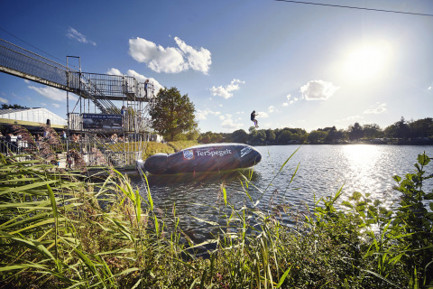 Diversión en el lago en Recreatiepark TerSpegelt WaterLodges Brabant, personas saltando desde una plataforma al agua.