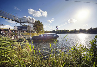 Sjov ved søen i Recreatiepark TerSpegelt WaterLodges Brabant med folk, der hopper fra en platform ned i vandet.
