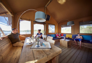 Family relaxing inside a glamping WaterLodge at Recreatiepark TerSpegelt, Brabant, with lake views outside.