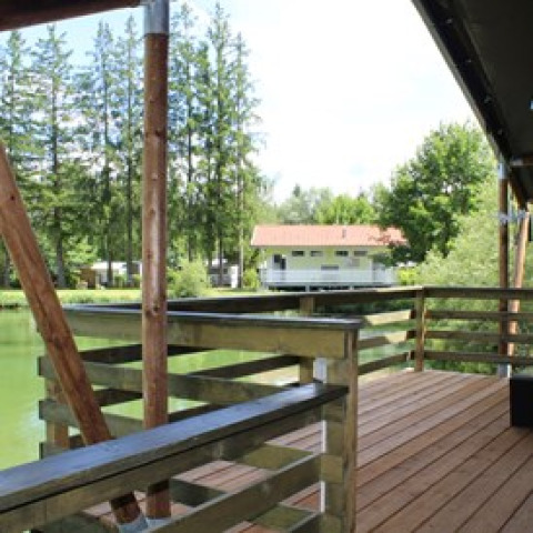 Terraza de madera con vista al lago y árboles en Camping Ammertal - Lodges Beieren, ideal para glamping.