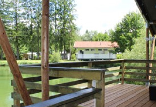 Træterrasse med udsigt over en sø og skov ved Camping Ammertal - Lodges Beieren, ideel til glamping.