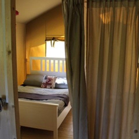 Indgang til hyggeligt glamping-soveværelse med dobbeltseng, gardin og varme trætoner hos Camping Ammertal.