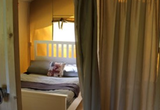 Entrance to a cozy glamping bedroom with a double bed, curtain, and warm wood tones at Camping Ammertal.