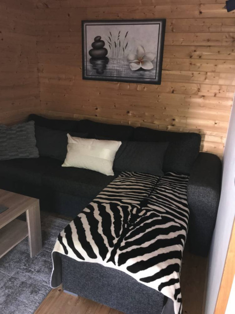Modern glamping lodge at Camping Ammertal featuring wood walls, dark sofa, and zebra blanket in Bavaria.