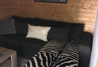 Moderne glamping-lodge ved Camping Ammertal med trævægge, mørk sofa og zebradyne i Bayern.