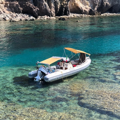 Un bateau pneumatique avec auvent ancré dans une eau claire près de rochers, Lavita Camp Cagliari.