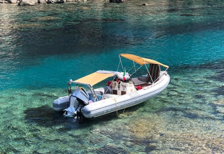 Opblaasbare boot met zonnescherm ligt voor anker in helderblauw water, Lavita Camp Cagliari, Sardinië.
