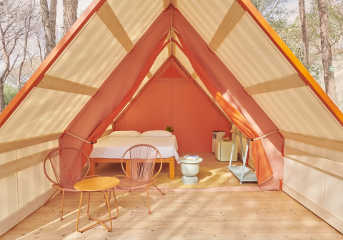 Lavita Camp Cagliari glamping tent in Sardinia with cozy bed, modern chairs, and forest surroundings.