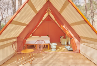 Lavita Camp Cagliari glamping tent in Sardinia with cozy bed, modern chairs, and forest surroundings.