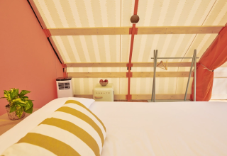 Intérieur d'une tente Lavita Camp Cagliari avec lit confortable, coussin rayé et décoration chaleureuse.