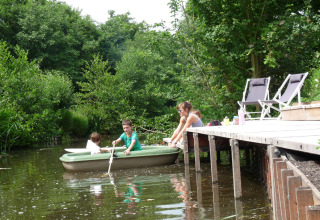 Enfants ramant dans une petite barque près d'un ponton en bois, avec adultes et verdure aux Pays-Bas.