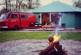 Glamping-ophold ved De Vreemde Vogel i Zuid-Holland med rød bil, grøn hytte og et lejrbål i forgrunden.