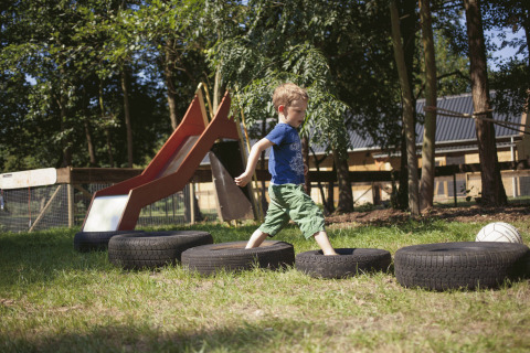 A child plays on car tires outdoors near a slide at De Vreemde Vogel, unique glamping in South Holland.