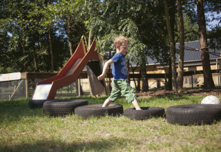 A child plays on car tires outdoors near a slide at De Vreemde Vogel, unique glamping in South Holland.