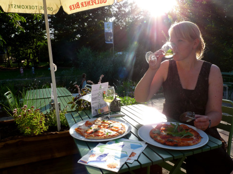 Vrouw geniet van wijn en pizza op het terras bij Glamping De Vreemde Vogel in zonnig Zuid-Holland.