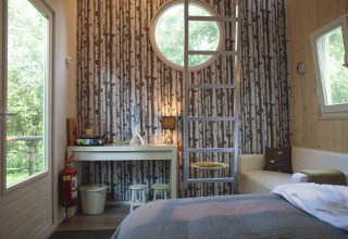 Modern glamping accommodation with round window, forest wallpaper, and cozy furnishings in Zuid-Holland.