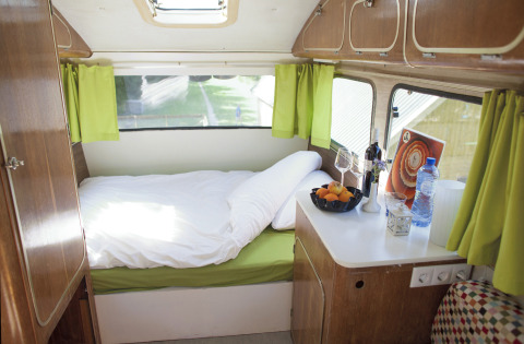 Cozy interior of a glamping caravan with a bed, green curtains, and countertop in South Holland.
