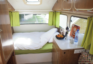 Cozy interior of a glamping caravan with a bed, green curtains, and countertop in South Holland.