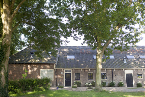 Außenansicht von De Vreemde Vogel, einzigartige Glamping-Unterkunft in Zuid-Holland mit Bäumen davor.