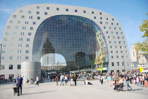 Moderne Markthal-bygning i Rotterdam, Holland, med glasfacade og mange besøgende foran en solrig dag.