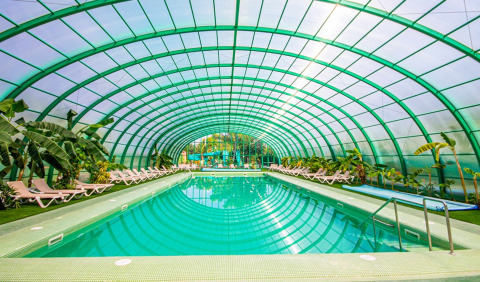 Überdachtes Schwimmbad mit Liegestühlen und tropischen Pflanzen im Camping & Resort La Torre del Sol, Costa Dorada.