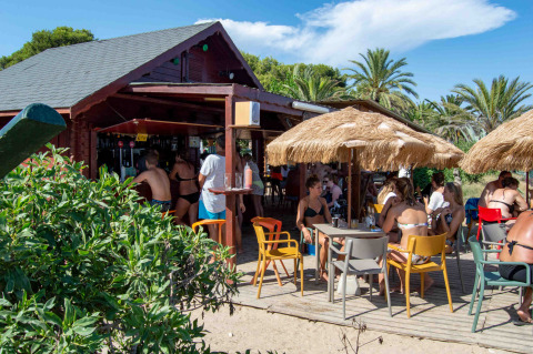 Bar sulla spiaggia al Camping & Resort La Torre del Sol, tavoli sotto ombrelloni e palme attorno.