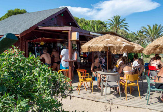 Terraza junto a la playa en Camping & Resort La Torre del Sol, bar con sombrillas y sillas de colores.