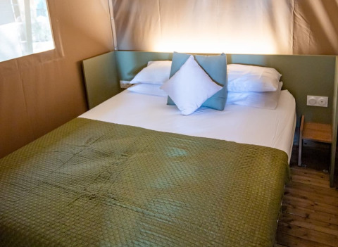 Gemütliches Bett mit grüner Decke und Kissen im Safarizelt bei Camping & Resort La Torre del Sol, Costa Dorada.