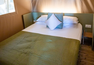 Gemütliches Bett mit grüner Decke und Kissen im Safarizelt bei Camping & Resort La Torre del Sol, Costa Dorada.
