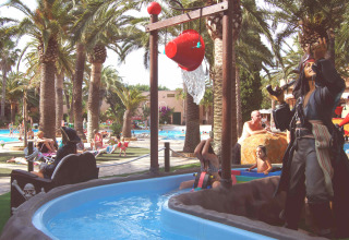 Zona acuática temática pirata en Camping & Resort La Torre del Sol, con palmeras, piscina y bañistas.
