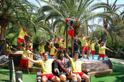 Et gruppefoto af unge voksne i gule trøjer ved en pool, omgivet af palmer på Camping & Resort La Torre del Sol.