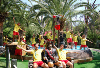 Grupo de jóvenes con camisetas amarillas posando junto a la piscina y palmeras en Camping & Resort La Torre del Sol.