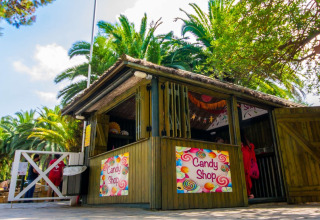 Colorful outdoor candy shop at Camping & Resort La Torre del Sol - Safaritenten Costa Dorada, surrounded by palm trees.