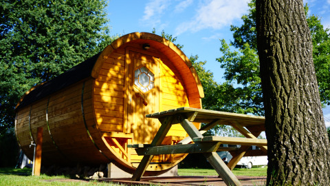 Rund træhytte i glampingstil med bænk foran, omgivet af grønne træer på Camping Heidekamp i Tyskland.