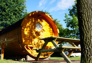 Alloggio glamping tondo in legno con tavolo da picnic, circondato da alberi al Camping Heidekamp.