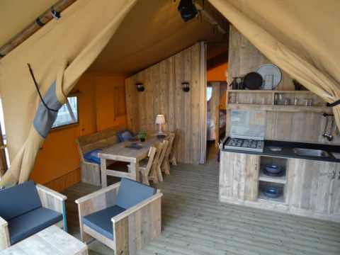 Vista interior de una glamping lodge en Camping Heidekamp, con muebles de madera y cocina integrada.