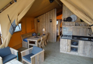 Interior view of a glamping lodge at Camping Heidekamp featuring wooden furniture and a compact kitchen.