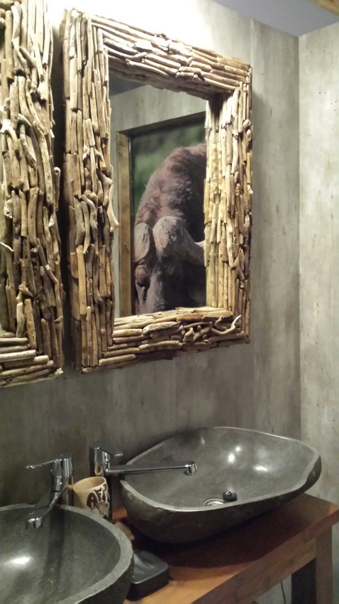 Baño con lavabos de piedra y espejo de madera que refleja una imagen de un búfalo al fondo.
