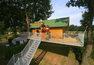 Unieke boomhut glamping accommodatie bij Kampeerbos de Simonshoek met een groot terras en trapopgang.