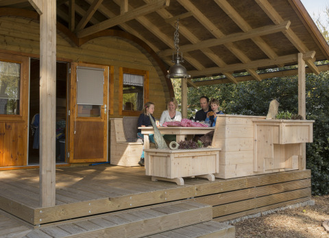Gezin geniet op de overdekte veranda van een houten lodge bij glamping Kampeerbos de Simonshoek.