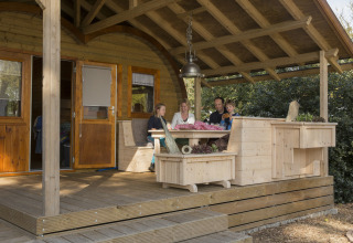 Famiglia rilassata sulla veranda coperta di una baita in legno presso il glamping Kampeerbos de Simonshoek.