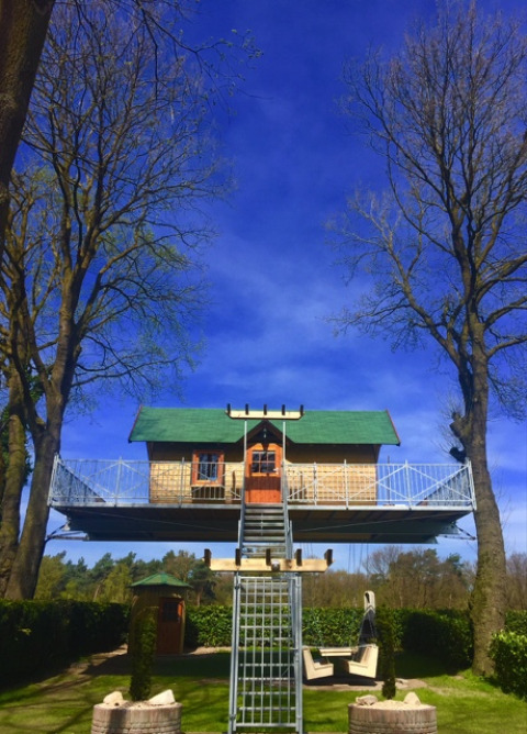 Glamping boomhut met groen dak op Kampeerbos de Simonshoek, tussen bomen en onder een blauwe lucht.